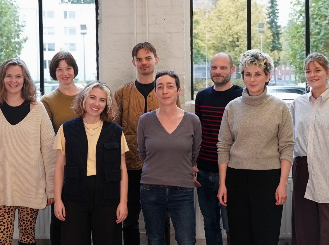 Auf dem Foto sind 8 Personen abgebildet, die am K3 arbeiten. Sie stehen vor einem großen Fenster.